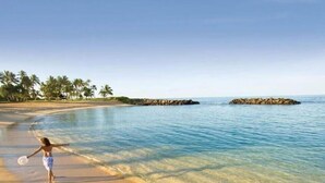 A beach with clear water, a person playing with a frisbee, and palm trees in the background. - Stunning Ocean View Luxury Suite - Ko Olina Beach Villas O421 End Unit (Kapolei)