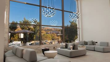 A modern living room with large windows, a stone wall, and a view of a mountainous landscape.