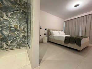 A modern bedroom with a bed, a nightstand, a wall-mounted light, and a shower area with a glass door.