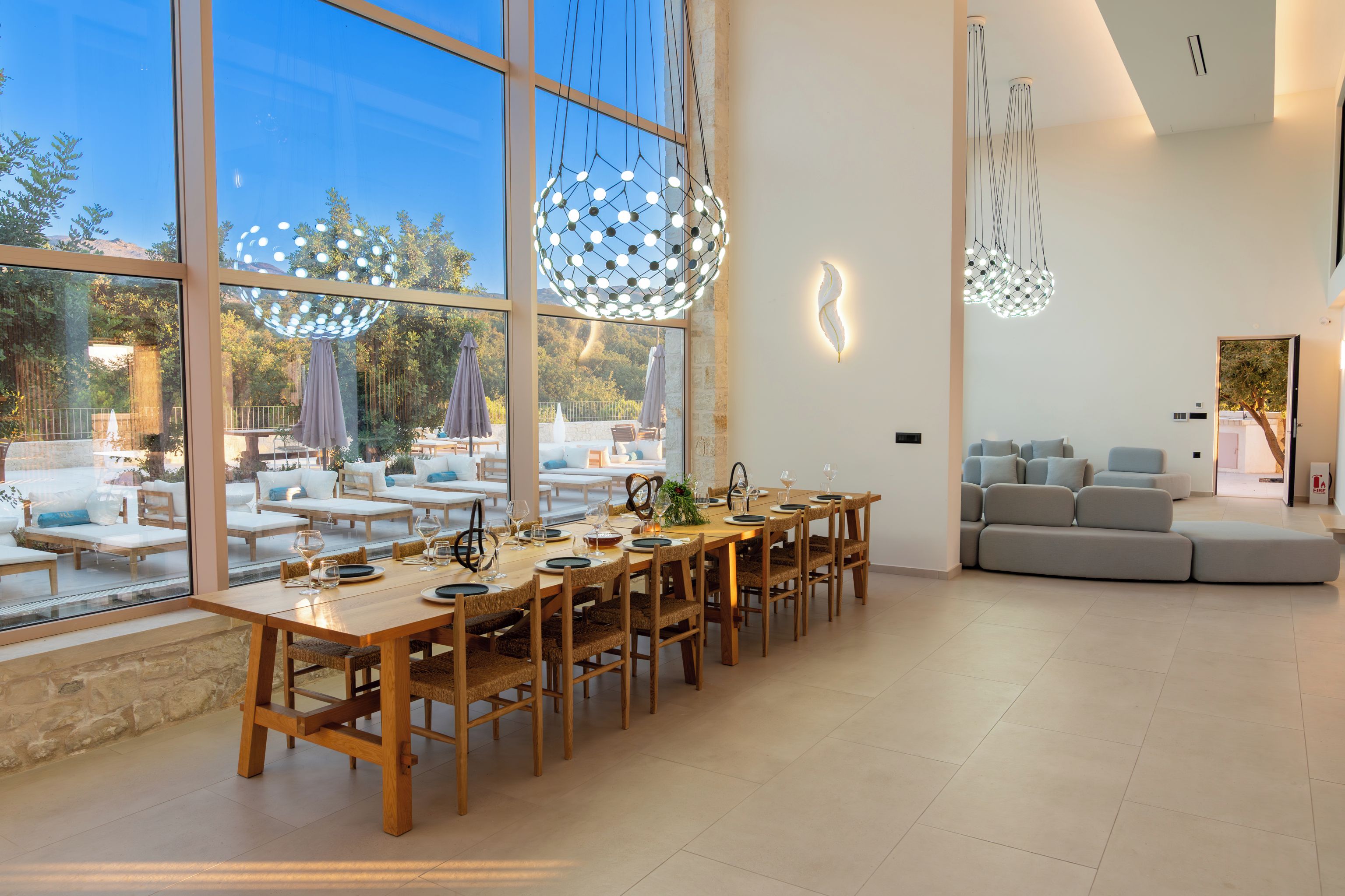 A dining area with a long wooden table set for a meal, large windows offering a view of the outdoors, and a modern interior design.