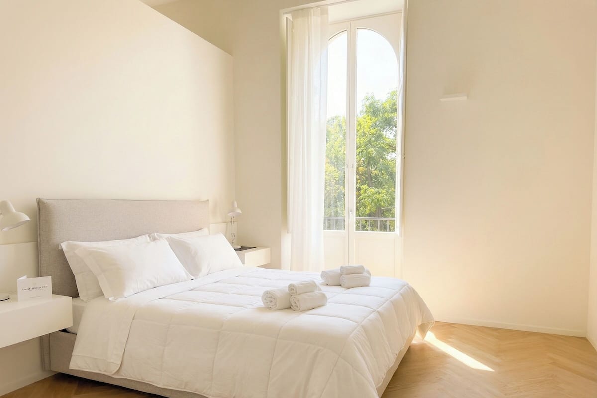 Une chambre à coucher avec un lit, des tables de chevet, une fenêtre donnant sur des arbres et un plancher en bois.