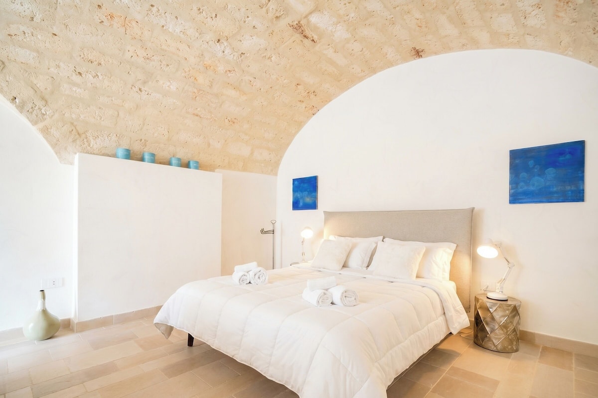 Une chambre à coucher avec un lit, une table de chevet, une lampe fixée au mur et deux tableaux bleus.