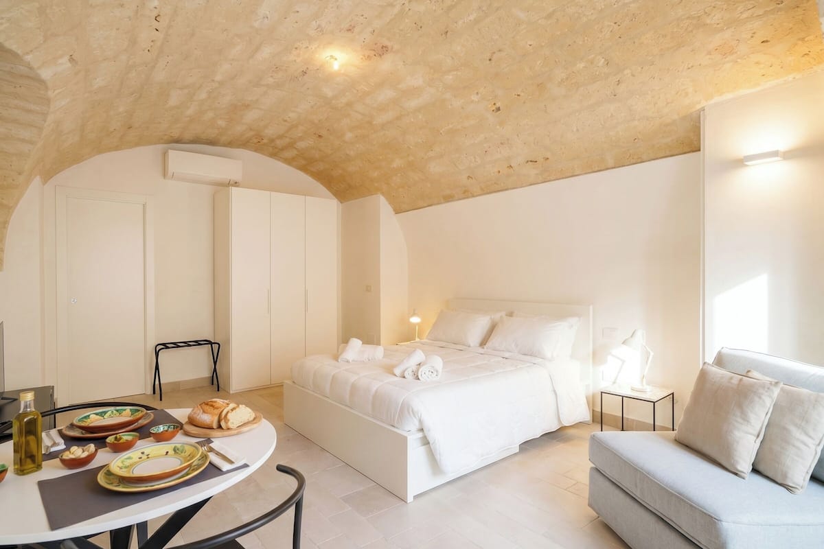 Une chambre avec un lit, un canapé, une table avec des assiettes et du pain, et un coin repas.