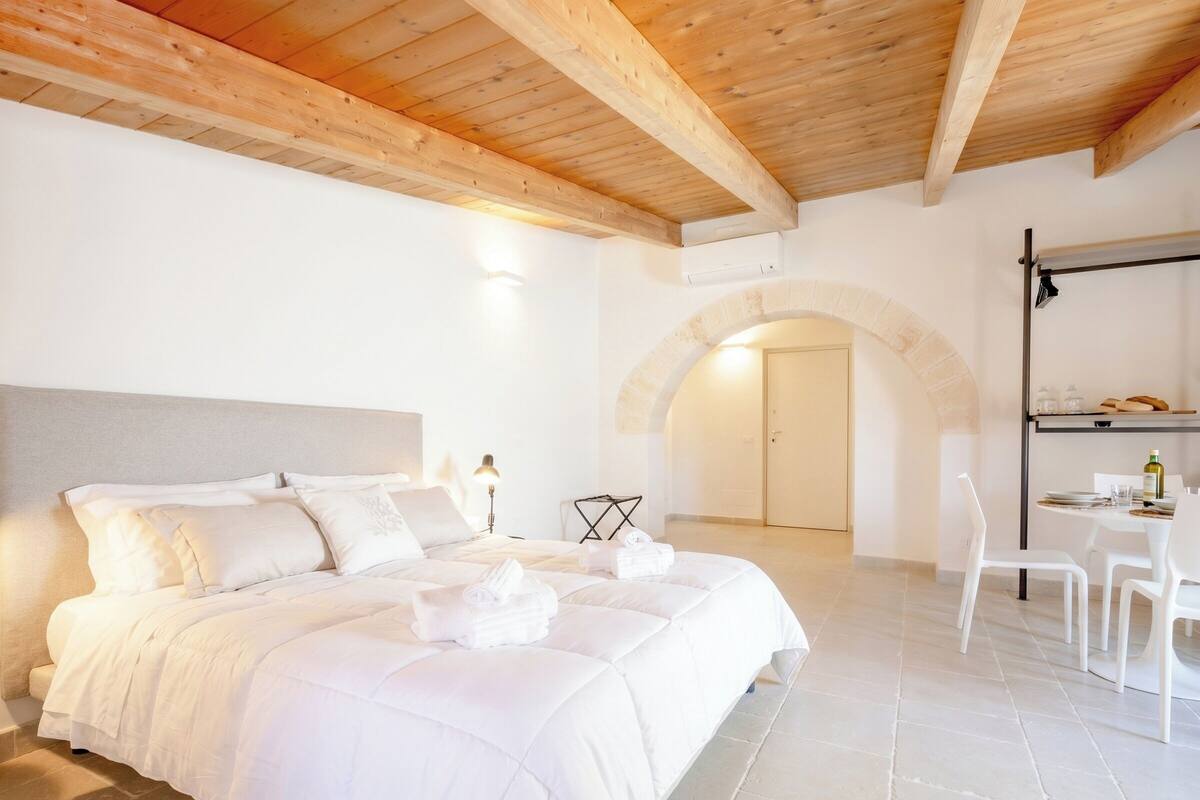 Une chambre à coucher avec un lit, un bureau avec des chaises, une lampe et une porte en arc de cercle.