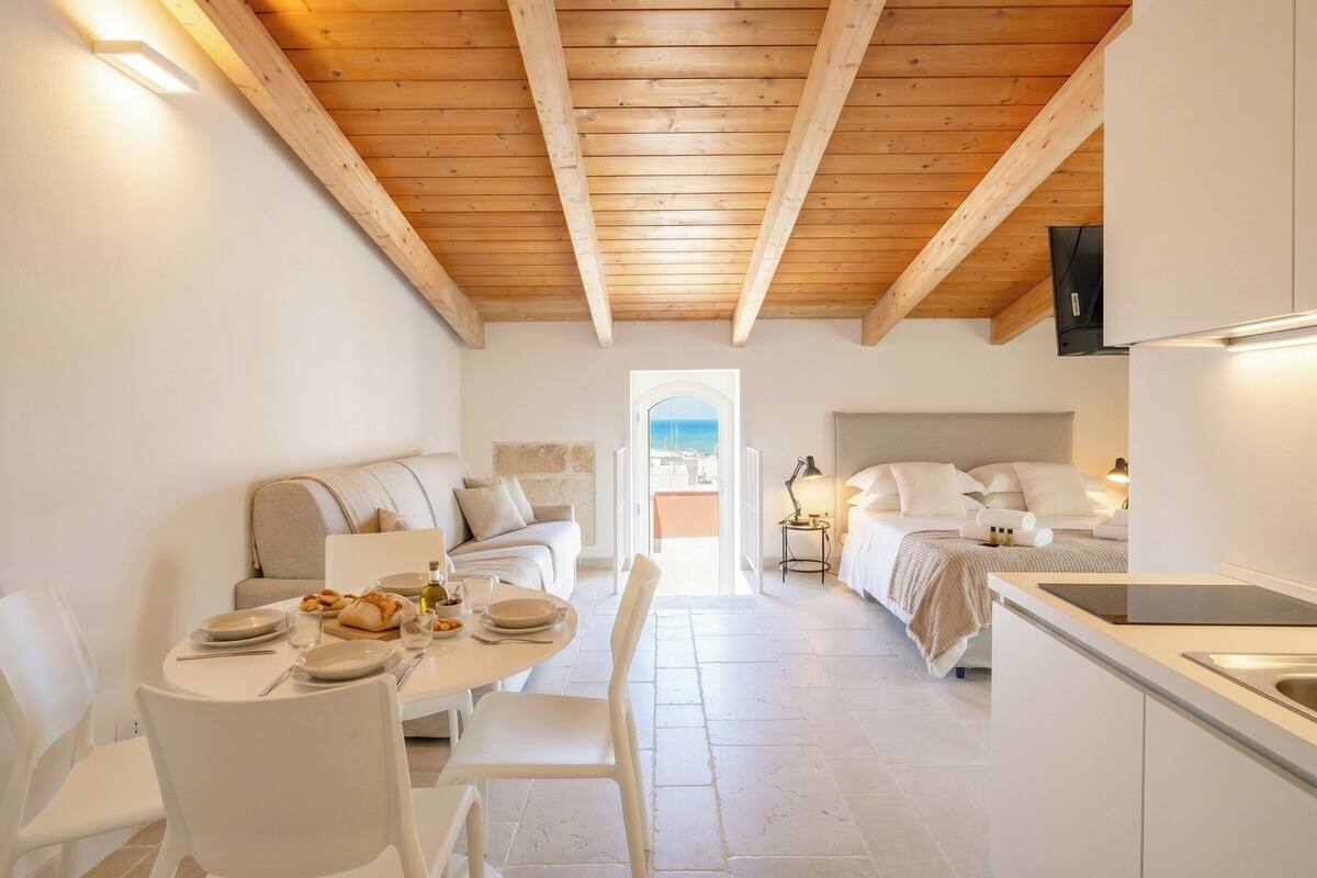 Un intérieur moderne avec un plafond en bois, un coin repas avec une table dressée pour deux personnes, un canapé et un lit offrant une vue agréable.
