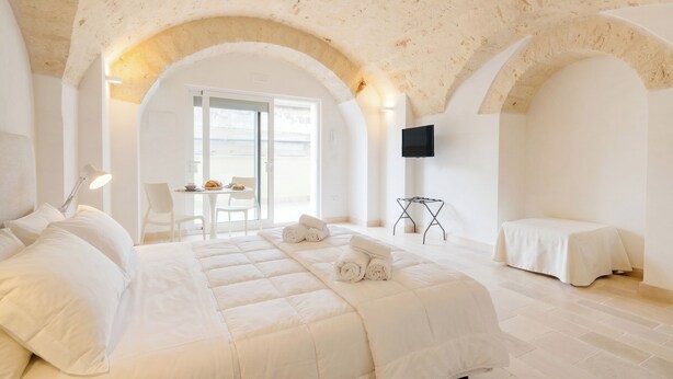 Ein Schlafzimmer mit einem großen Bett, einem Schreibtisch mit Stuhl, einem Fernseher und einem Balkon.