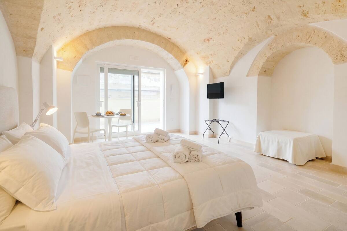 Une chambre avec un grand lit, un bureau avec une chaise, une télévision et un balcon.