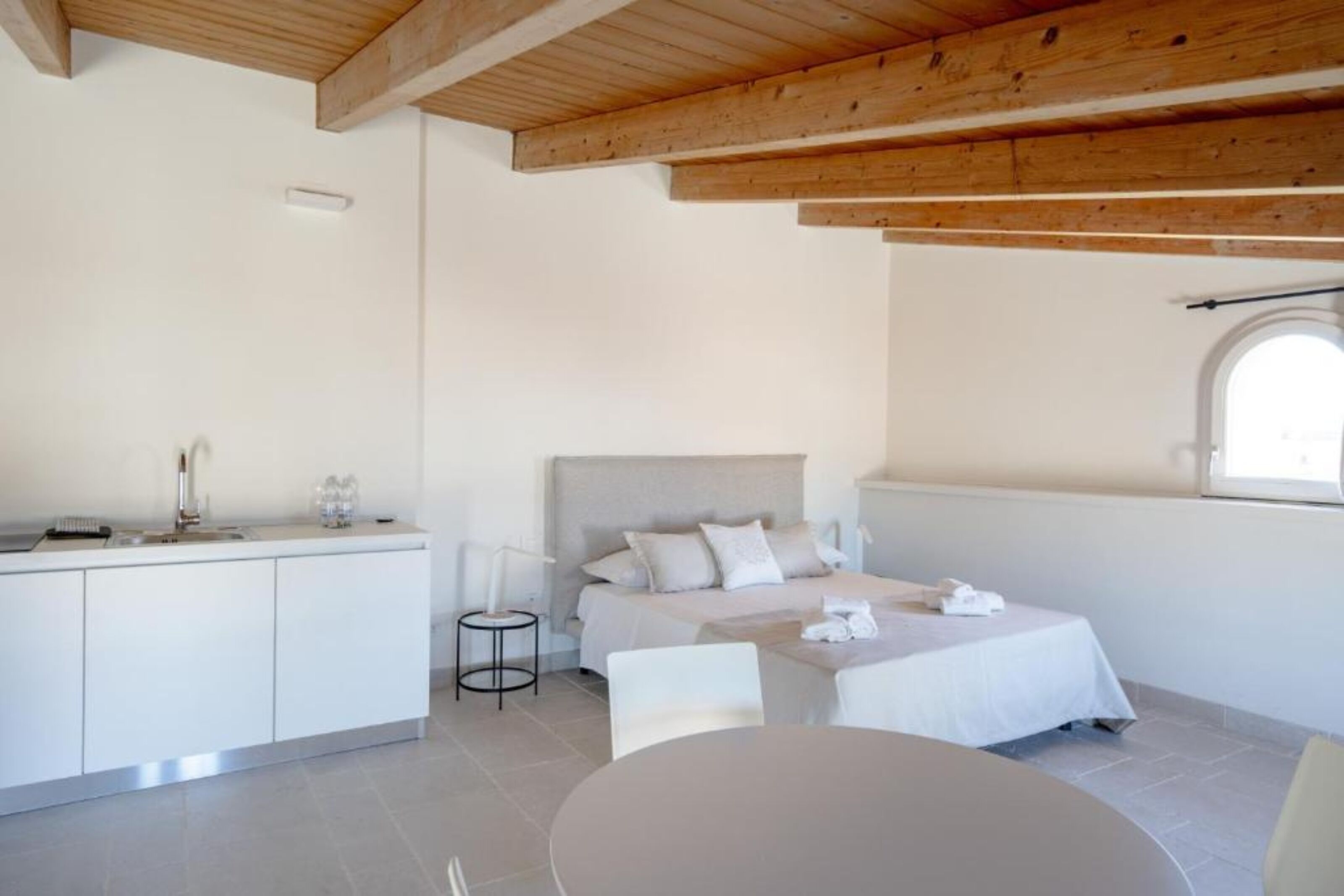 A modern bedroom with a large bed, a bedside table, a small desk, and a window with a view.