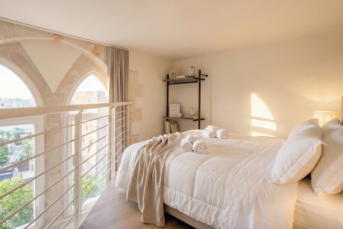 Une chambre à coucher avec un lit, une table de chevet, une étagère avec divers objets et une vue par la fenêtre.