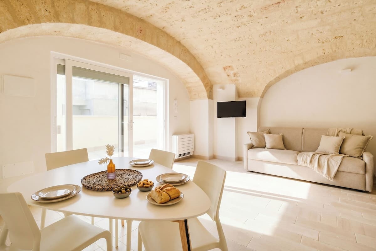 Un coin repas avec une table dressée pour quatre personnes, un canapé et un téléviseur fixé au mur.