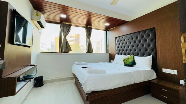 A modern hotel room with a large bed, a ceiling fan, a TV mounted on the wall, and a window with curtains. - artus inn midc andheri east mumbai (Mumbai)