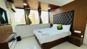 A modern hotel room with a large bed, wooden headboard, and a view of buildings outside the window. - artus inn midc andheri east mumbai (Mumbai)