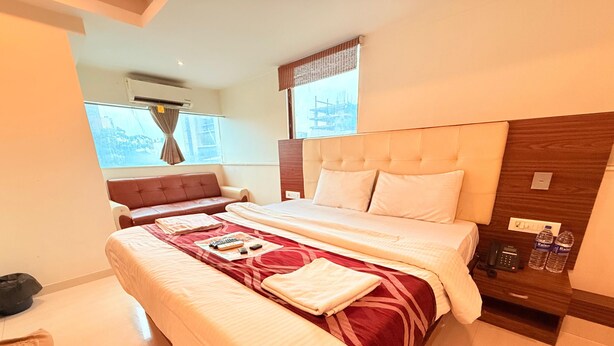 A hotel room with a large bed, a sofa, a wooden nightstand, and a window with curtains. - artus inn midc andheri east mumbai (Mumbai)