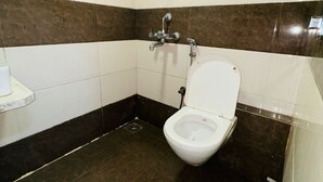 A small, tiled bathroom with a white toilet, a showerhead, and a wall-mounted faucet. - artus inn midc andheri east mumbai (Mumbai)