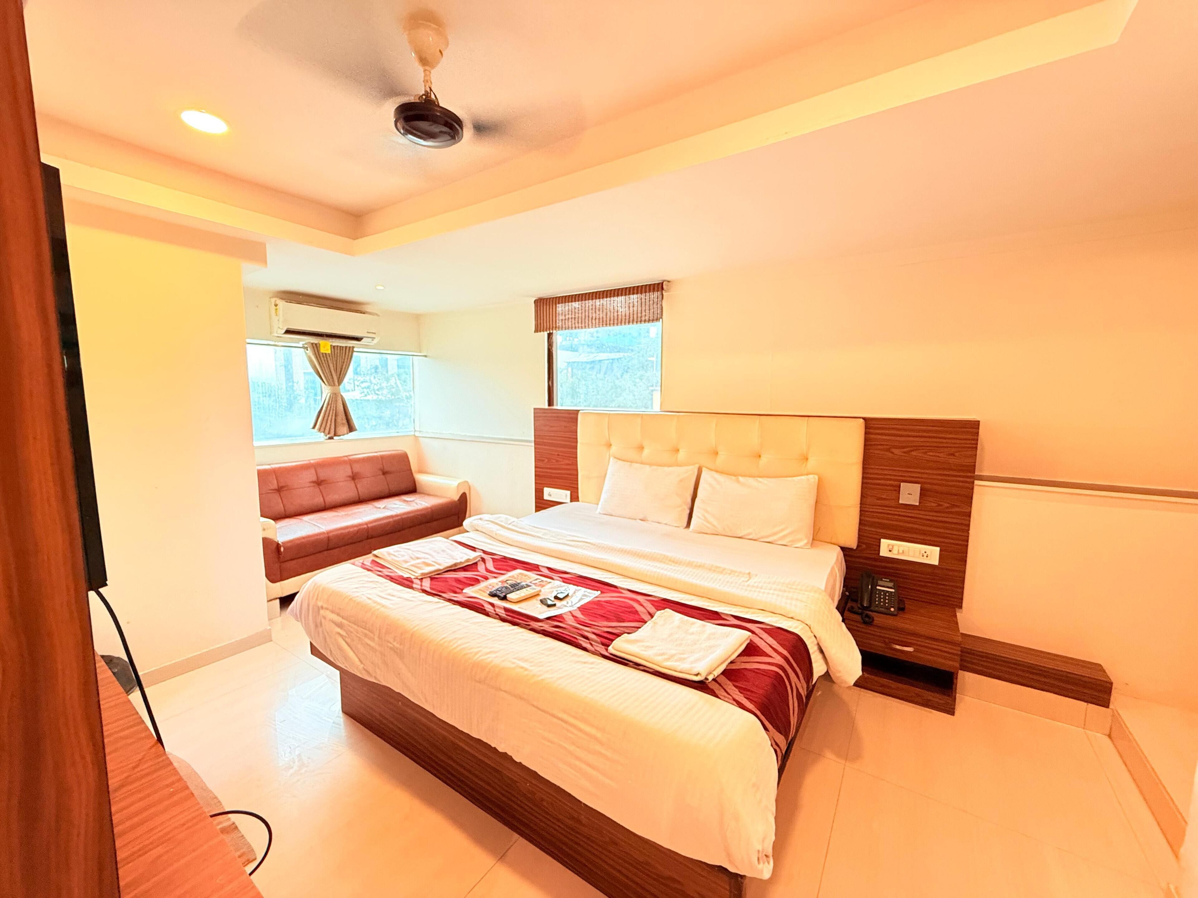 A hotel room with a large bed, a sofa, a ceiling fan, and a window with curtains.