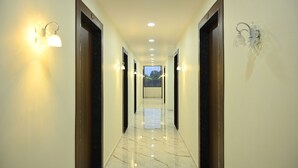 A hotel hallway with marble flooring, wooden doors, and wall-mounted light fixtures. - Hotel Vanvira (Mawal)