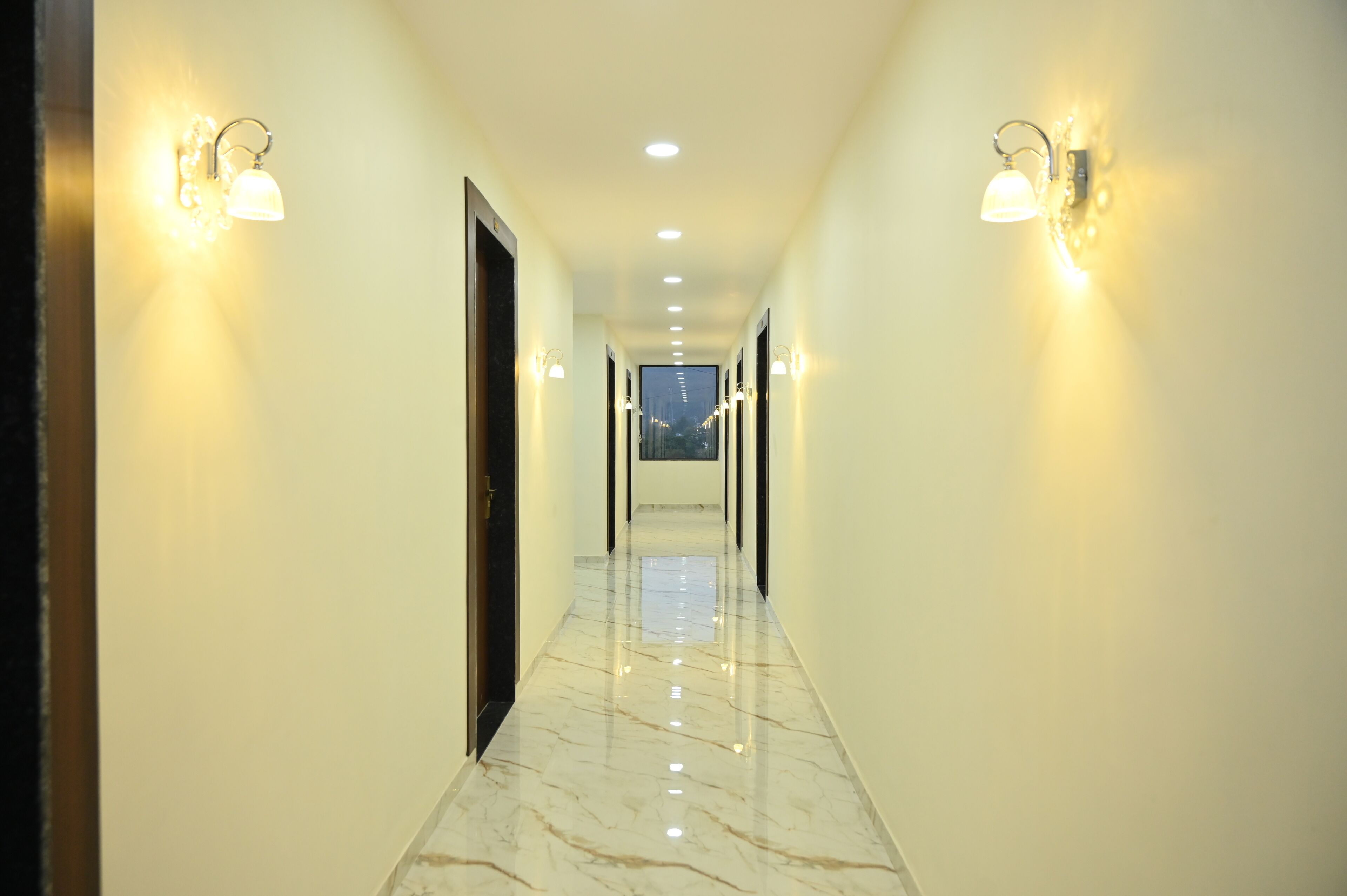 A long, well-lit hallway with marble flooring and wall-mounted lights.
