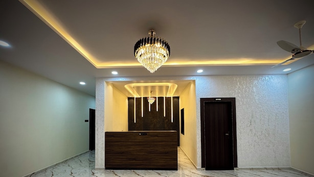 A modern reception area with a marble floor, a reception desk, a chandelier, recessed ceiling lights, and a ceiling fan. - Hotel Vanvira (Mawal)