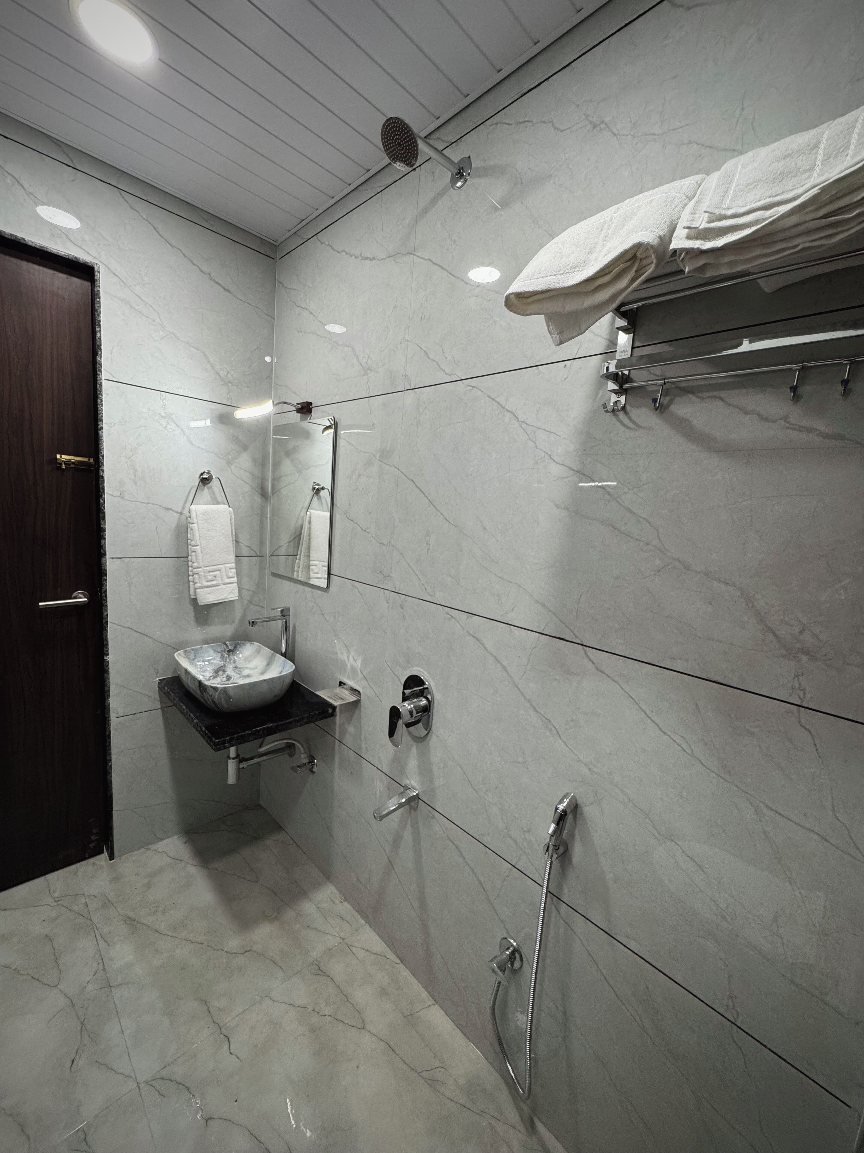 Un baño moderno con lavamanos de mármol, cabezal de ducha de mano y un perchero para toallas.