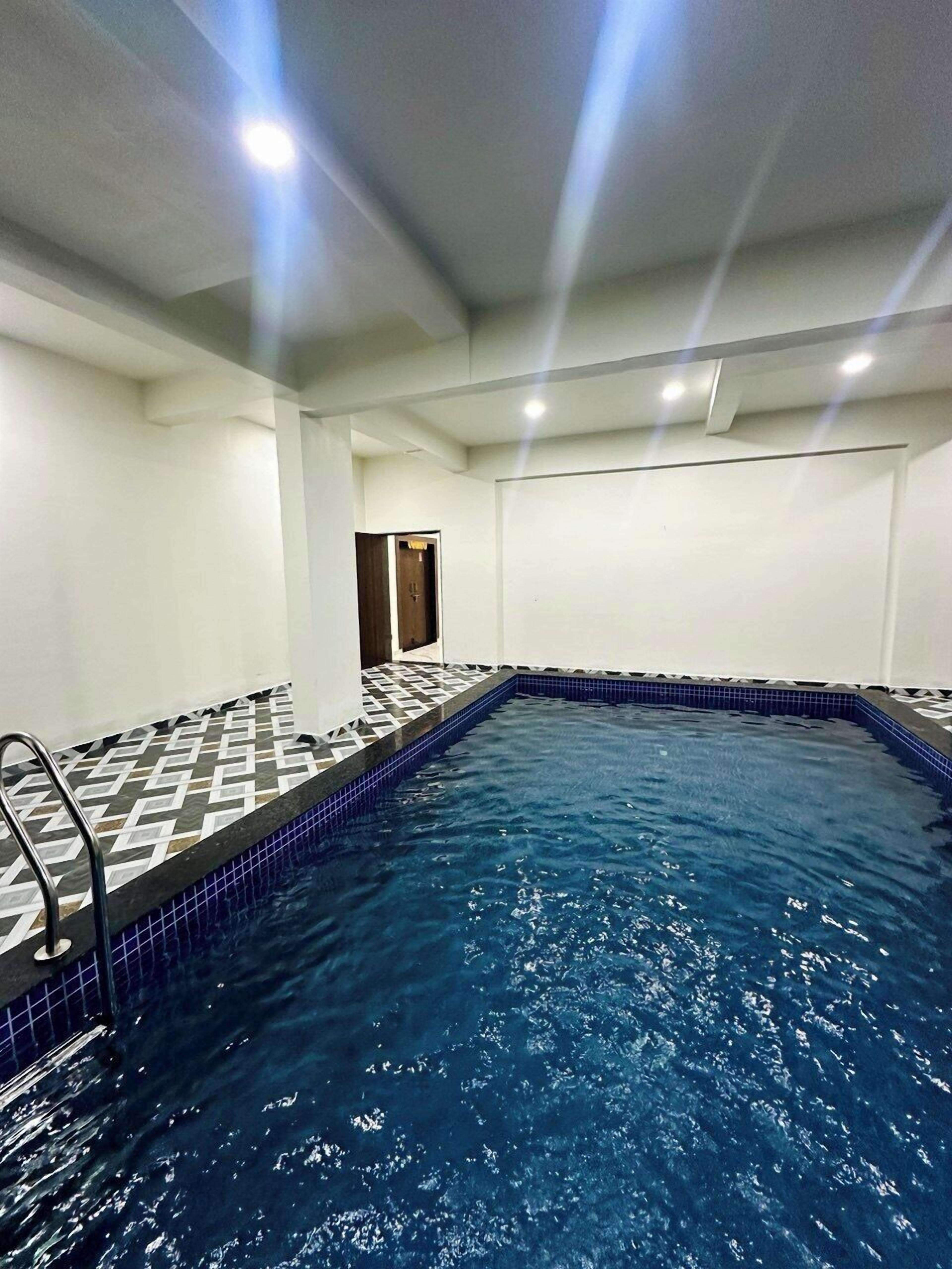 Uma piscina interna com um padrão geométrico de azulejos, uma escada e uma porta que dá para outro cômodo.
