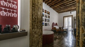 A room with a wooden ceiling, a red wall with wine glasses, a kitchen area, and a seating area with a table and chairs. - Ballarooms Experience (Palermo)
