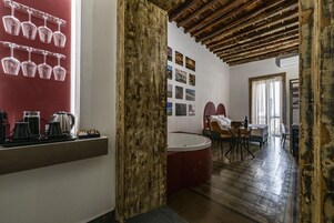 A room with a wooden ceiling, a red wall with wine glasses, a kitchen area, and a seating area with a table and chairs.
