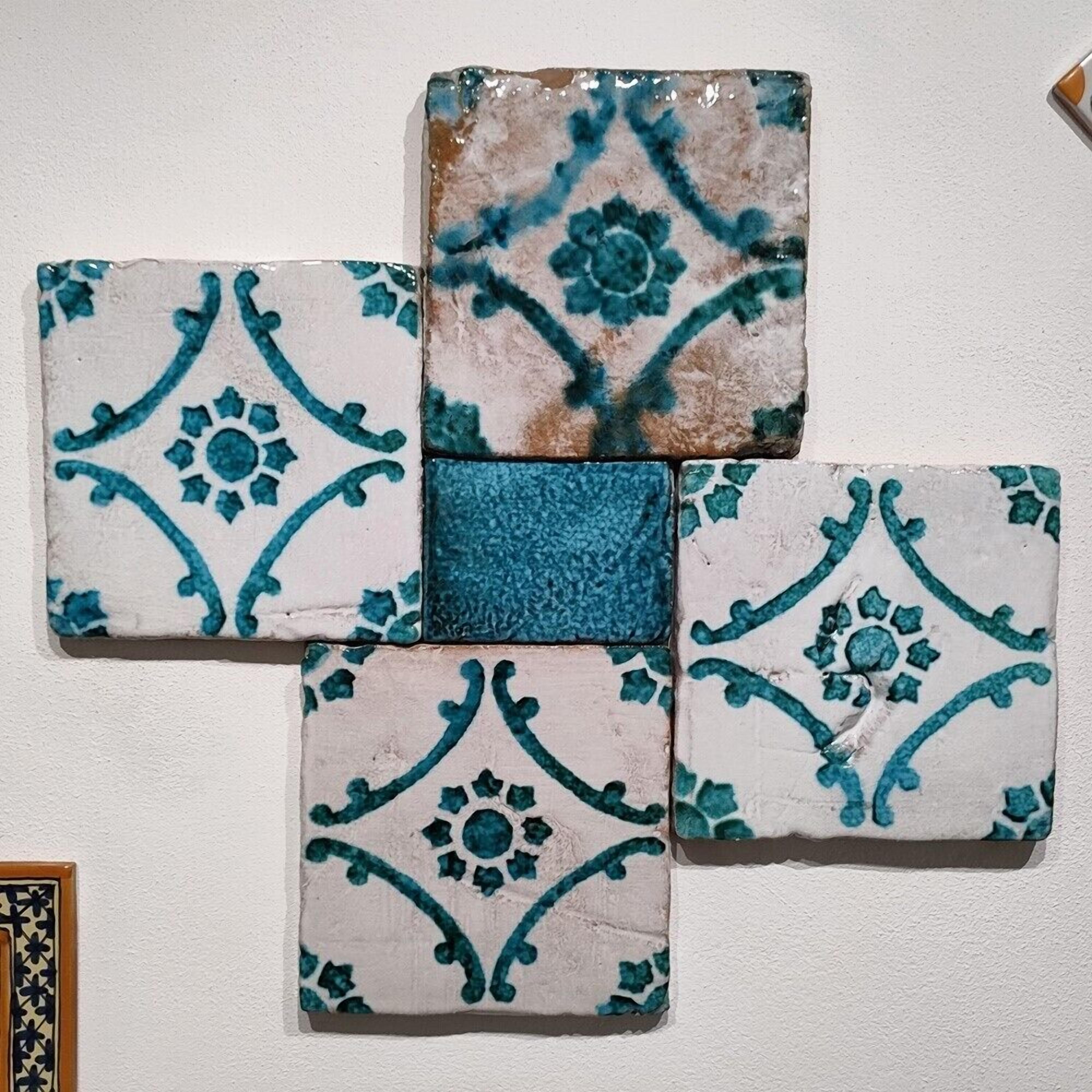 Four square tiles with blue patterns arranged on a wall.