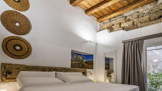 A bedroom with a wooden ceiling, a bed, a nightstand, a mirror, and a window with curtains. - Ballarooms Experience (Palermo)