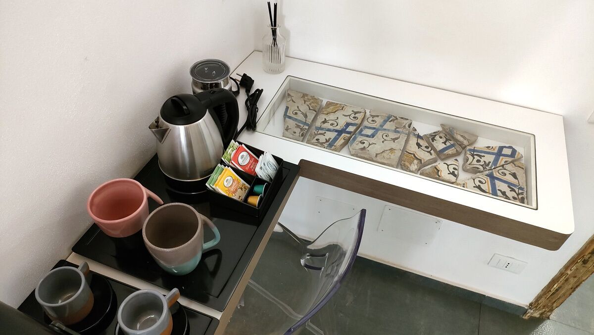 A kitchenette with a coffee maker, kettles, and a glass display case with pastries.