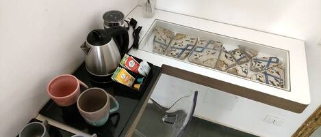 A kitchenette with a coffee maker, kettles, and a glass display case with pastries.