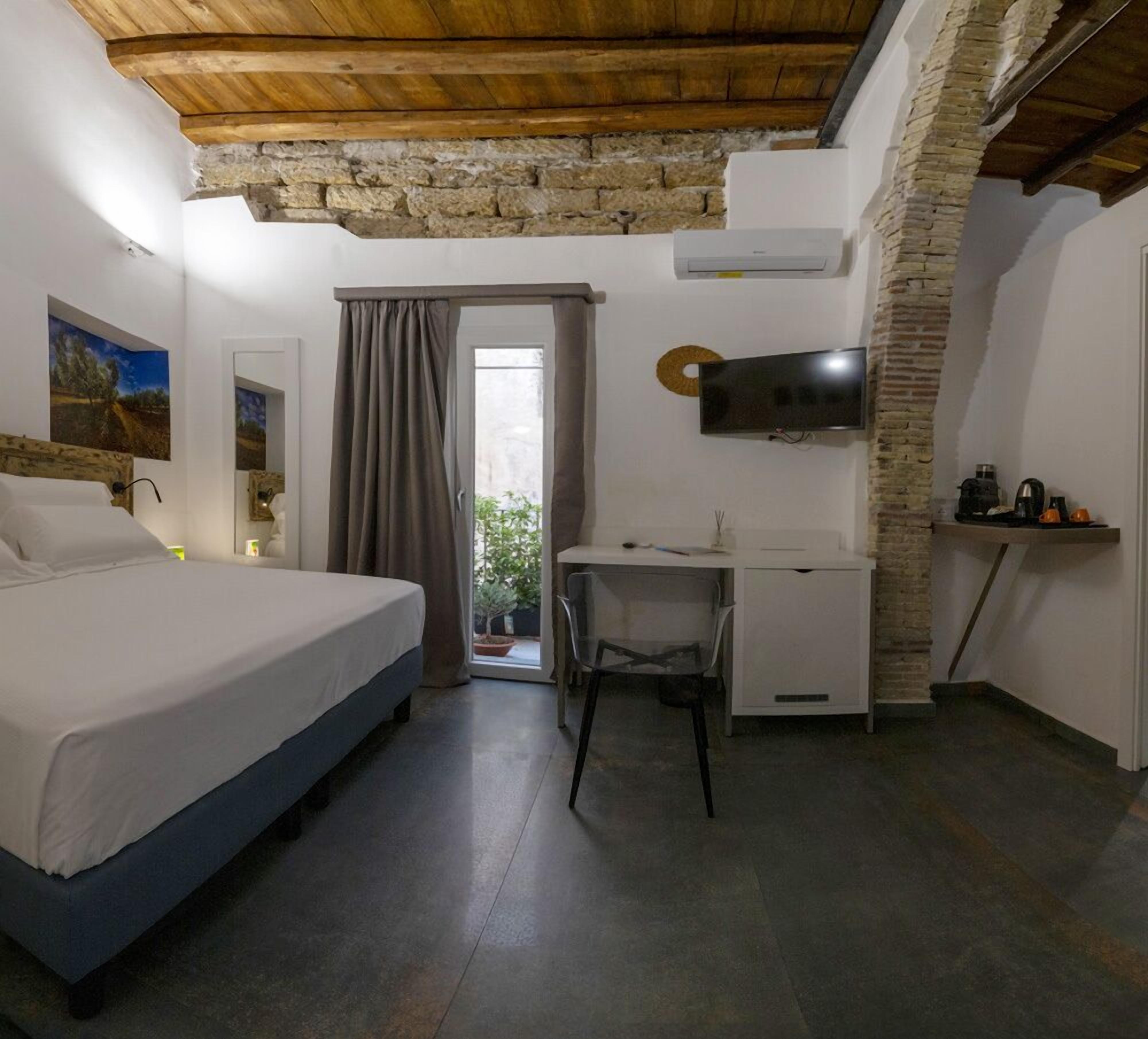 Una camera da letto con un letto, una scrivania, una TV e un muro in pietra.
