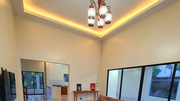 A modern living room with a large sectional sofa, a wooden coffee table, and a TV mounted on the wall. - Enjoyable 4-bedroom house with AC in Panglao (Panglao)