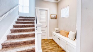A staircase with carpeted steps leading to a landing with a bench and a door.