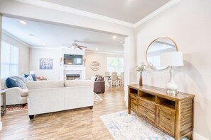 A spacious living room with a large sofa, wooden entertainment center, and a fireplace. - Walk-to-Stadium: 6BR Luxury Home w/ En-Suite Baths (Fayetteville)