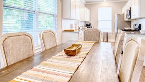 A dining area with a long wooden table, beige upholstered chairs, and a woven placemat.