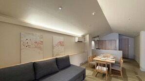 A modern living room with a grey sofa, a dining table set for four, and abstract wall art.