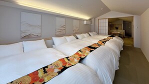 A hotel room with a long bed, a small dining area, and a view of the hallway.
