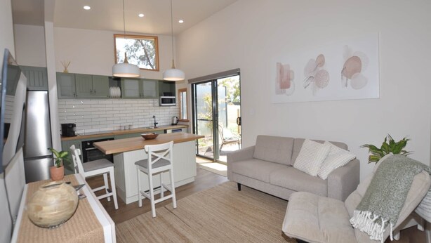 Eine moderne Küche mit weißen Schränken, ein Essbereich mit weißem Tisch und Stühlen, ein beiges Sofa und ein großes Fenster für natürliches Licht.