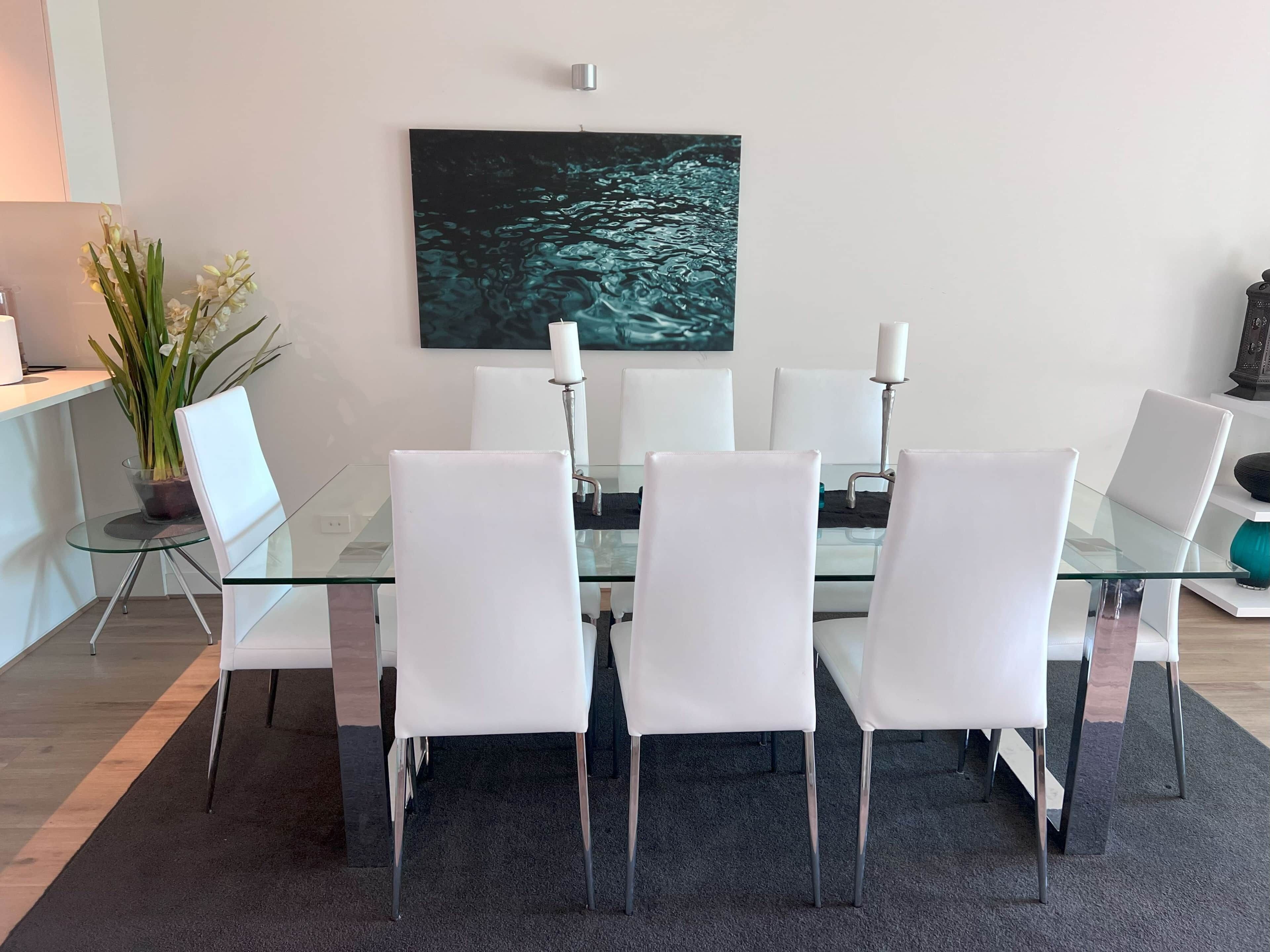 Un espace repas moderne avec une table en verre, des chaises blanches et un grand tableau abstrait accroché au mur.