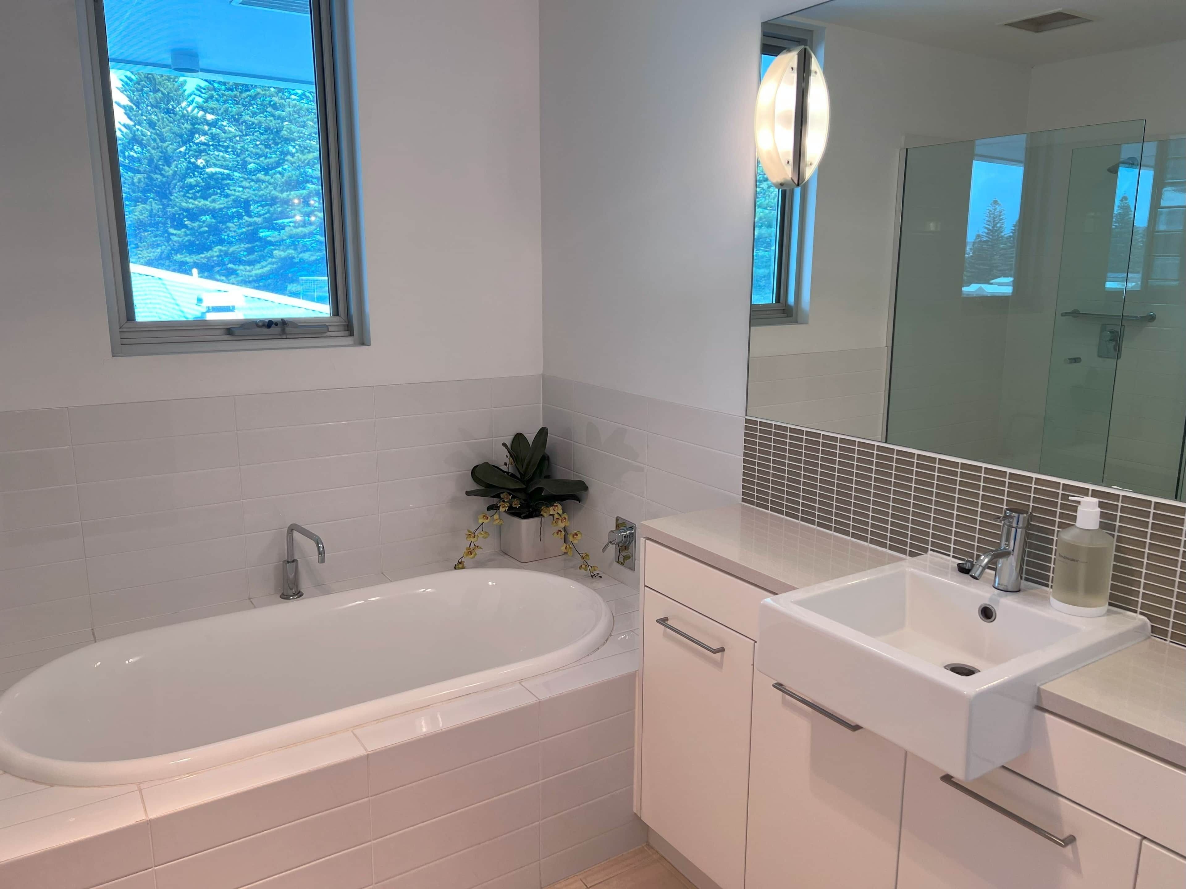 A modern bathroom with a bathtub, a sink, and a large mirror.