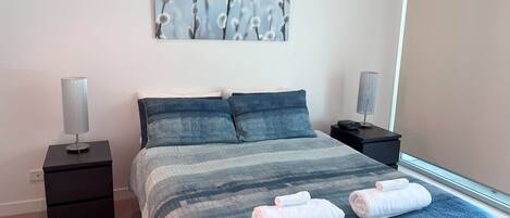 A neatly arranged bedroom with a bed, two bedside tables, a wall-mounted lamp, and a window.