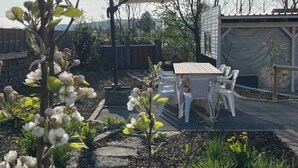 A patio area with a table and chairs, surrounded by a garden with flowering plants and a covered seating area. - Cozy vacation home (Biessenhofen)