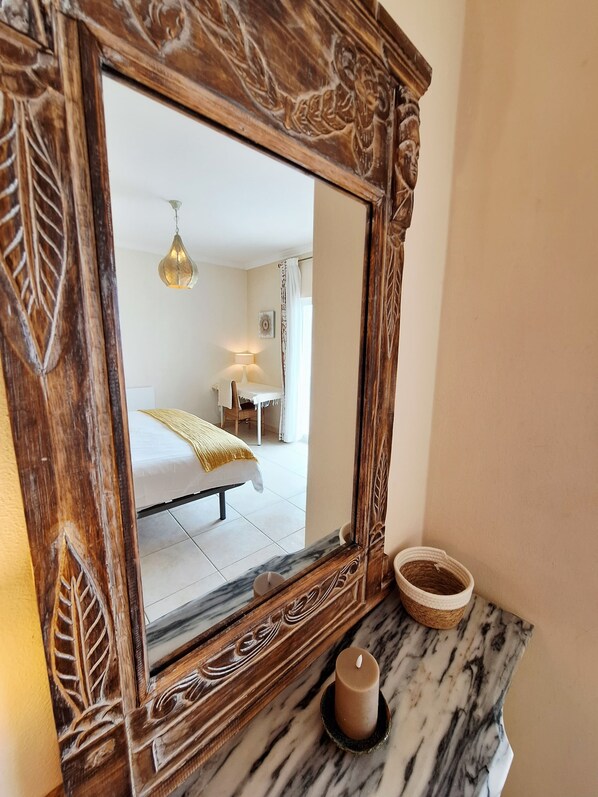 Un miroir orné de sculptures complexes, qui reflète une pièce comprenant un lit, une lampe et une fenêtre.