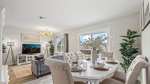 Un comedor con una mesa blanca dispuesta para cuatro personas, rodeada de sillas tapizadas en color beige.