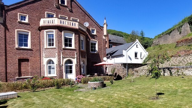 A large brick building with multiple windows and a balcony, surrounded by a well-maintained lawn and a smaller white building. - Vacation apartment "Beim alten Pfarrhaus" (Zell (Mosel))