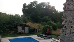A swimming pool with a stone border, surrounded by greenery and a rustic stone building.
