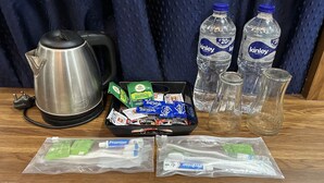Une table avec une bouilloire, des bouteilles d’eau, des sachets de thé, des brosses à dents et du dentifrice.