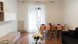 Un comedor con una mesa lista para cuatro personas, un sofá negro y un radiador.