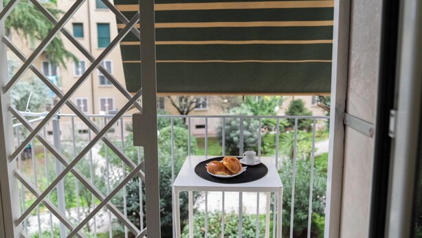 Un balcón con una mesa, una silla y vistas a edificios y zonas verdes.