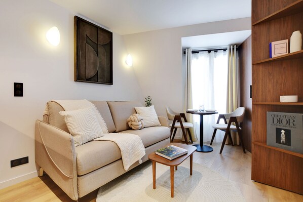 A modern living room with a beige sofa, a coffee table, and a bookshelf. - Modern Studio - 2P - AC - Madeleine/saint-lazare (Paris)